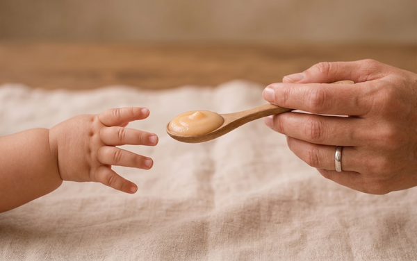 A baby reaching for a spoonful of food from an adult, illustrating why trust is the most important ingredient in children's food.